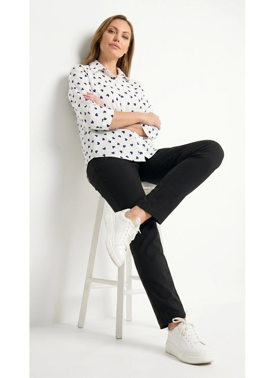 Woman sitting on a stool wearing a polka dot shirt, black pants, and white sneakers against a white background