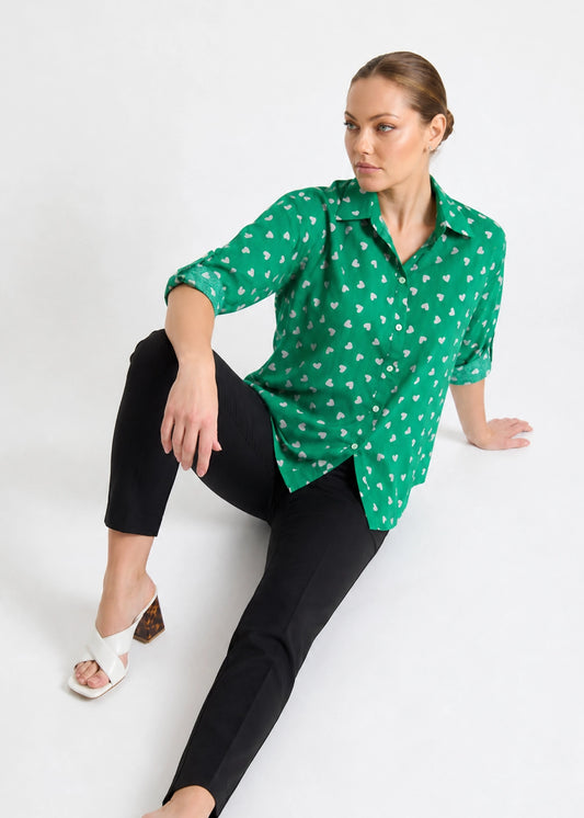 Woman wearing a green patterned blouse and black pants on a white background