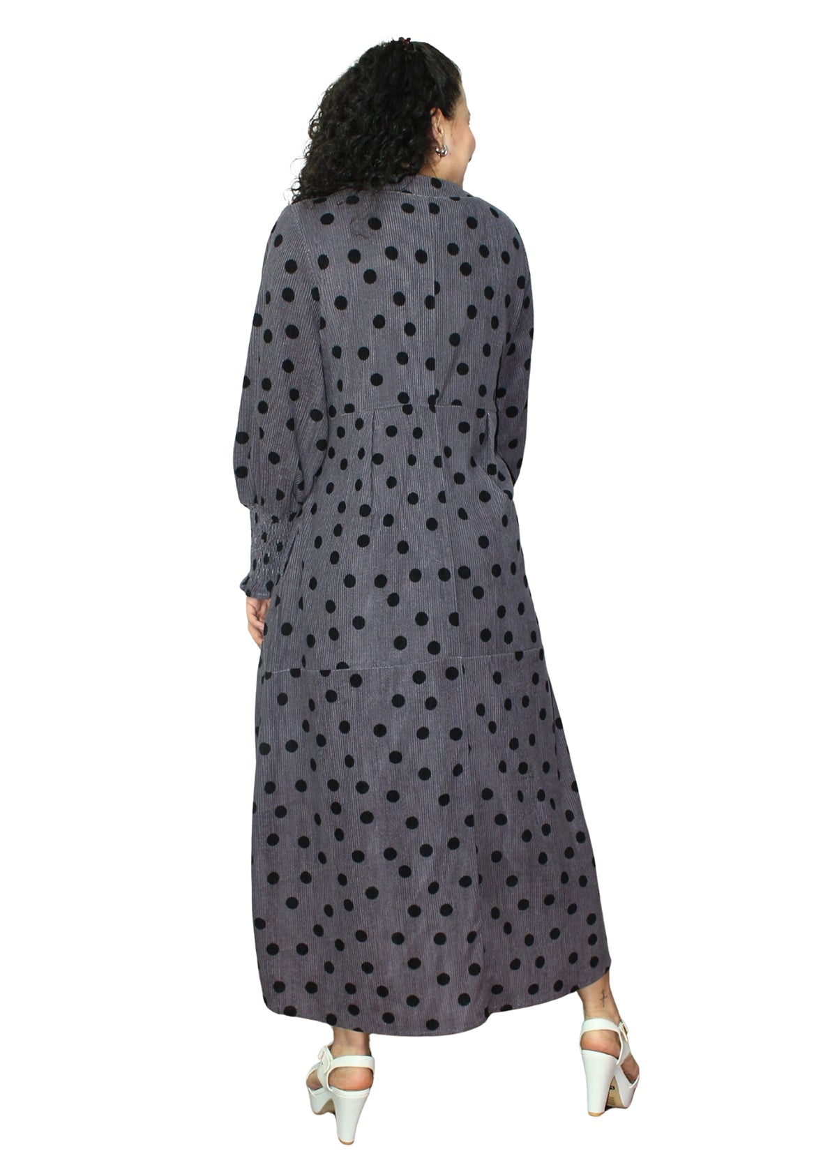 Woman wearing a long, dark gray dress with black polka dots on a white background