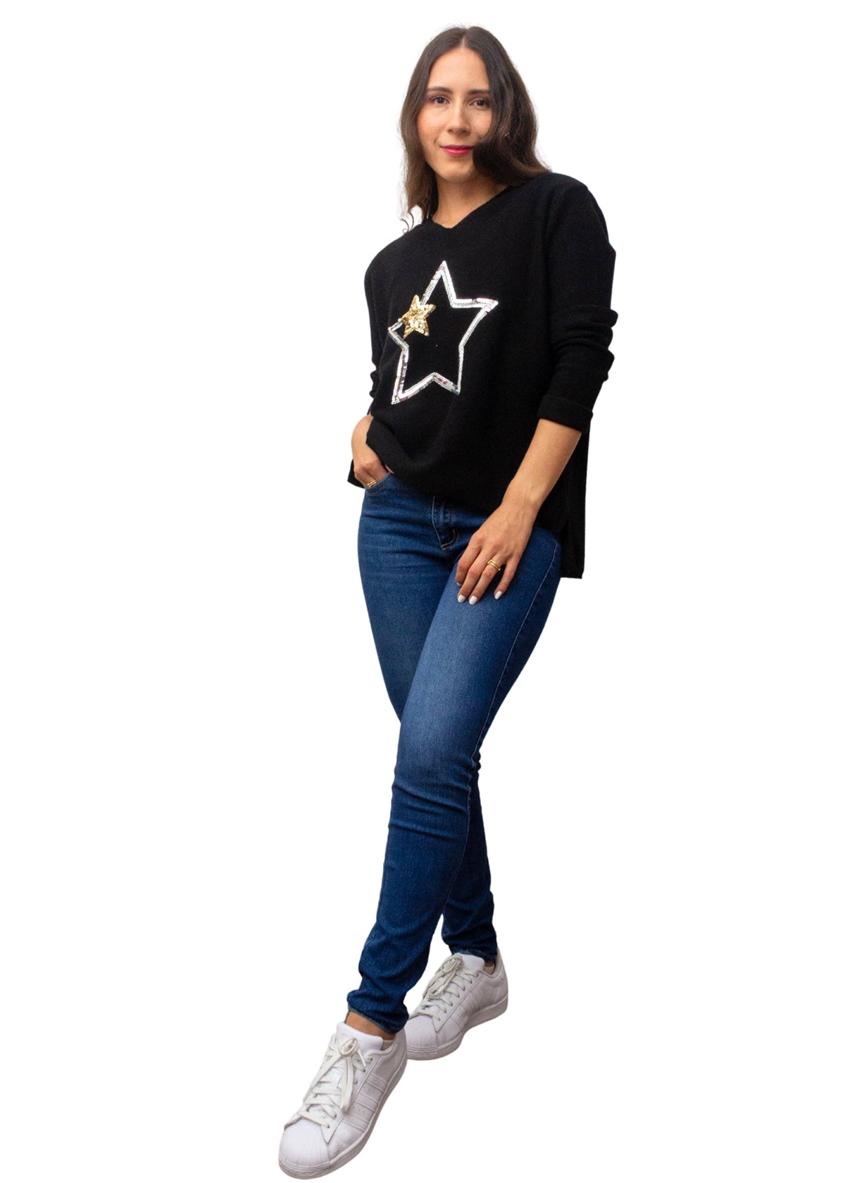 Woman wearing a black sweater with a star design, blue jeans, and white sneakers on a white background