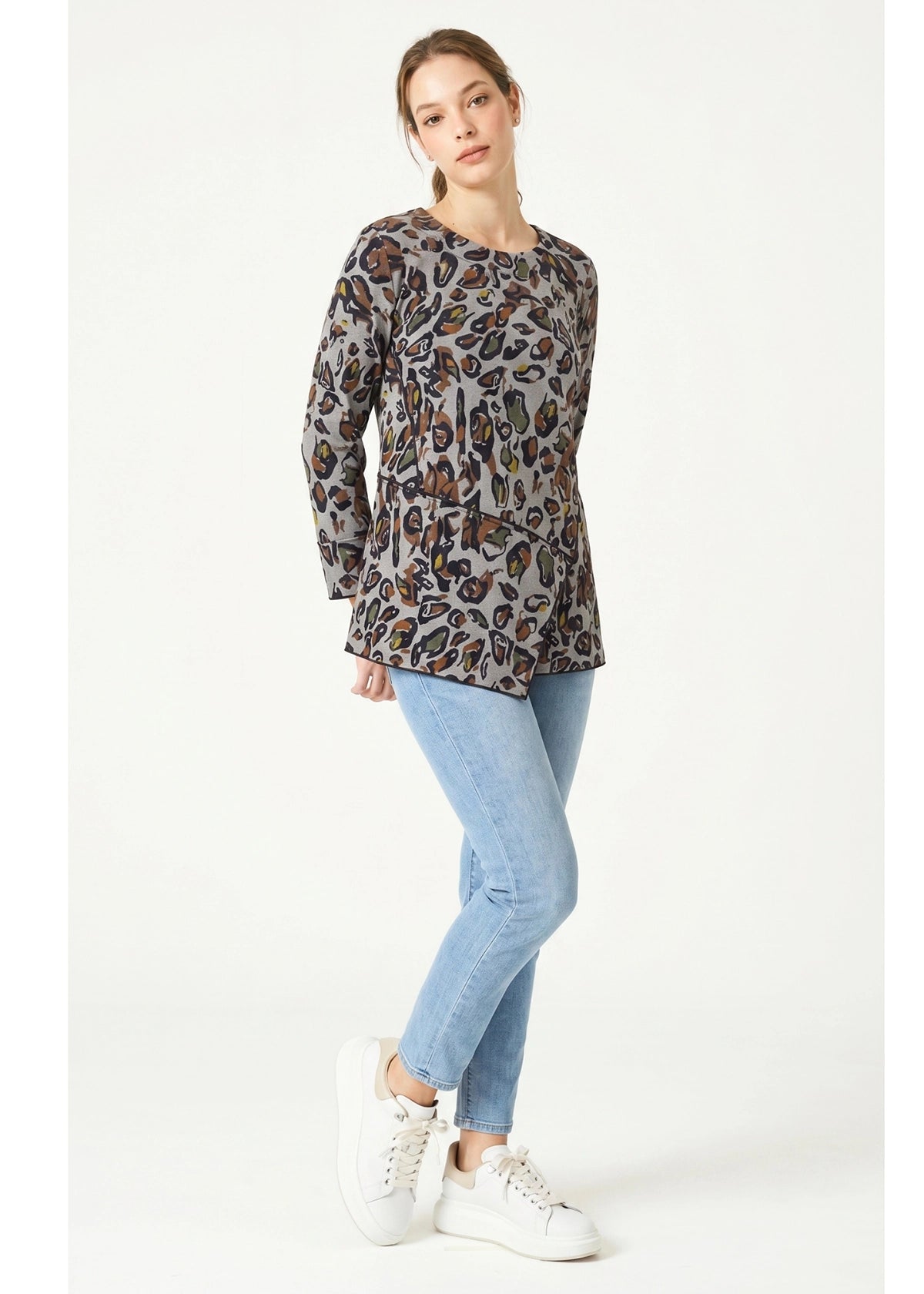 Woman wearing a leopard print top and light blue jeans on a white background