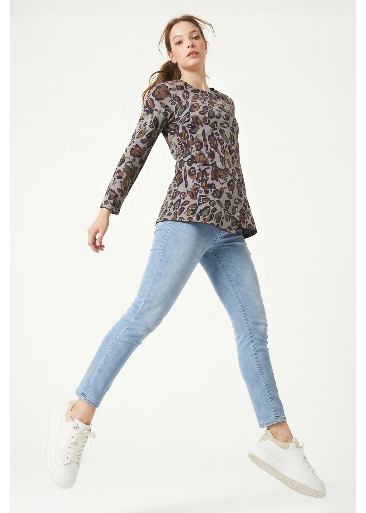 Woman wearing a patterned long-sleeve top and light blue jeans on a white background