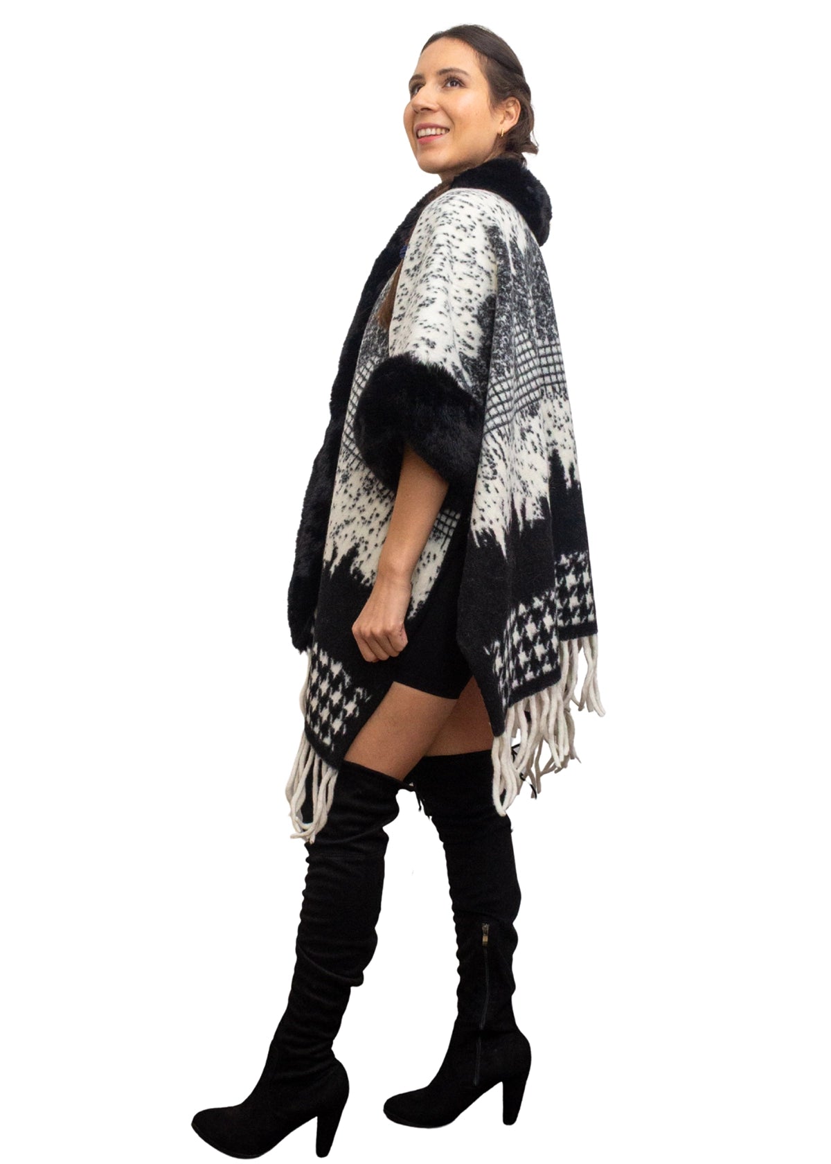 Woman wearing a black and white patterned poncho with fringe, standing against a white background.