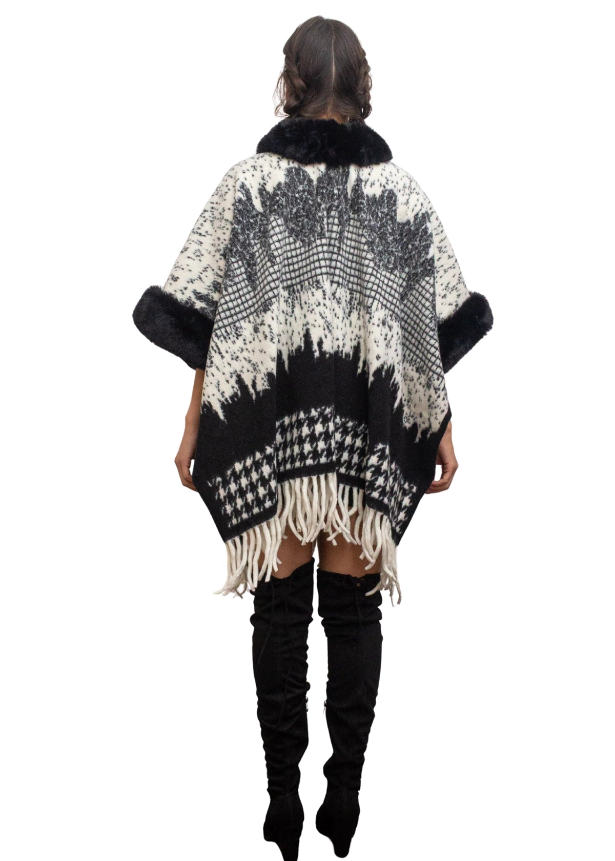 Person wearing a black and white patterned poncho with fringes on a white background