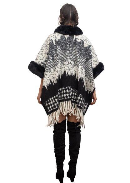 Person wearing a black and white patterned poncho with fringes on a white background